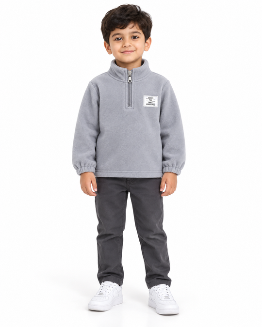 Boy wearing a cloud grey fleece half-zip sweatshirt with charcoal trousers and white sneakers.